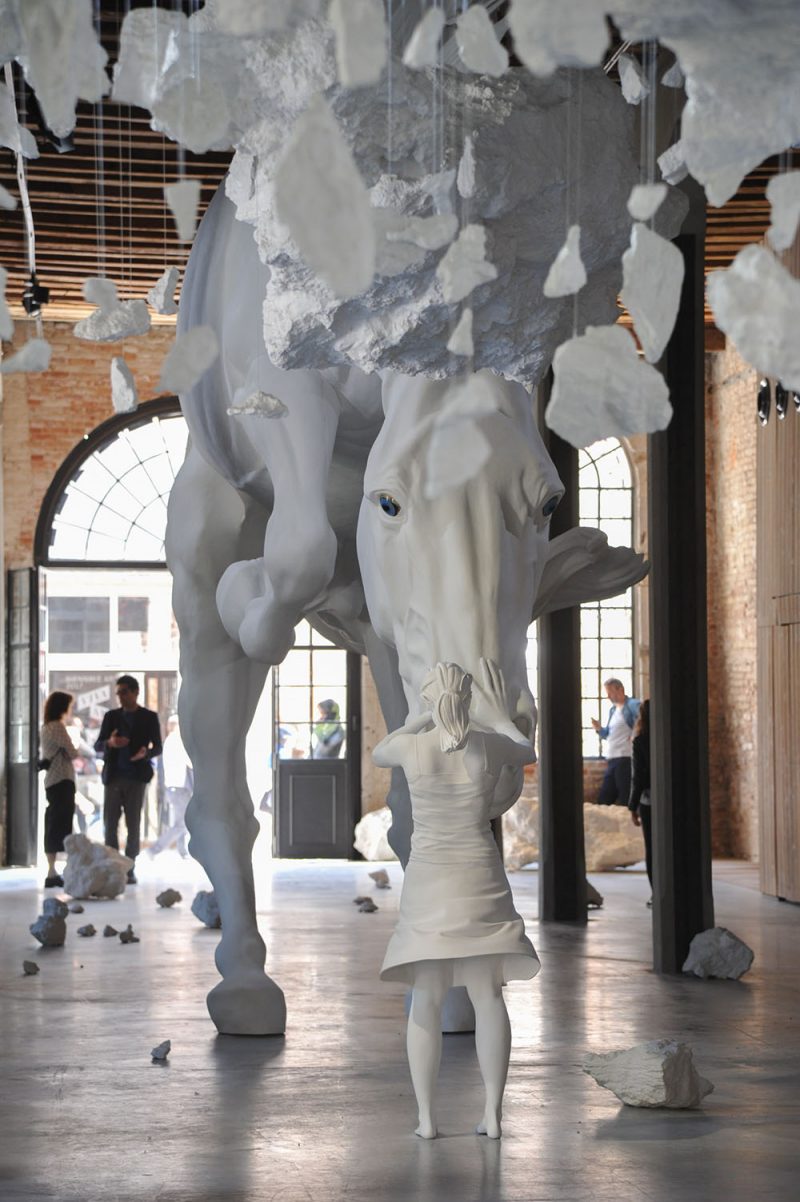 A girl encounters a giant white horse frozen in mid-air within the venice biennale’s Argentinian pavilion